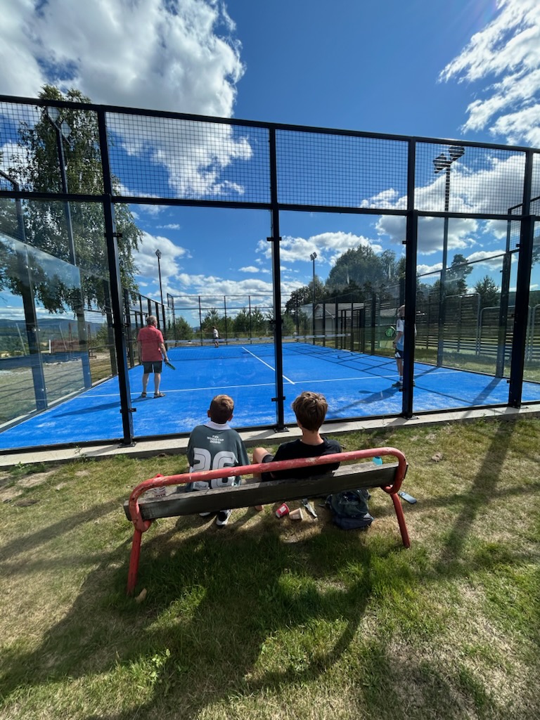 Spillere på padelbanen mens tilskuere ser på fra benken